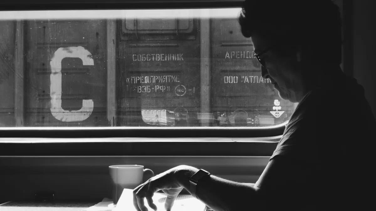 A woman reading a book on a train in black and white. Captivating light and shadow contrast.