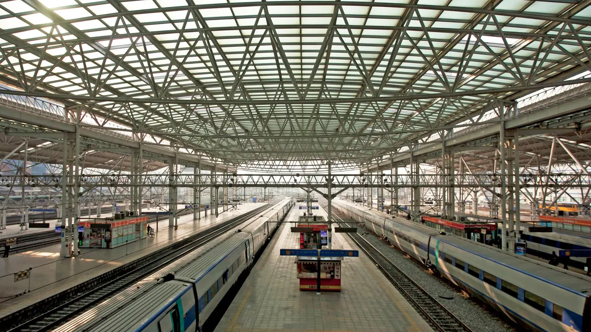 Spacious railway station with multiple platforms and trains under a steel glass roof.
