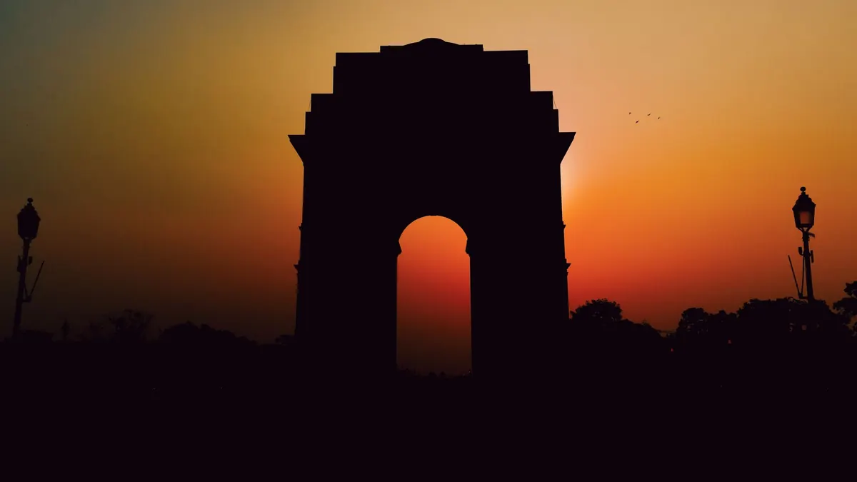Silhouette of India Gate against a vibrant sunset in New Delhi, India, highlighting its iconic structure.