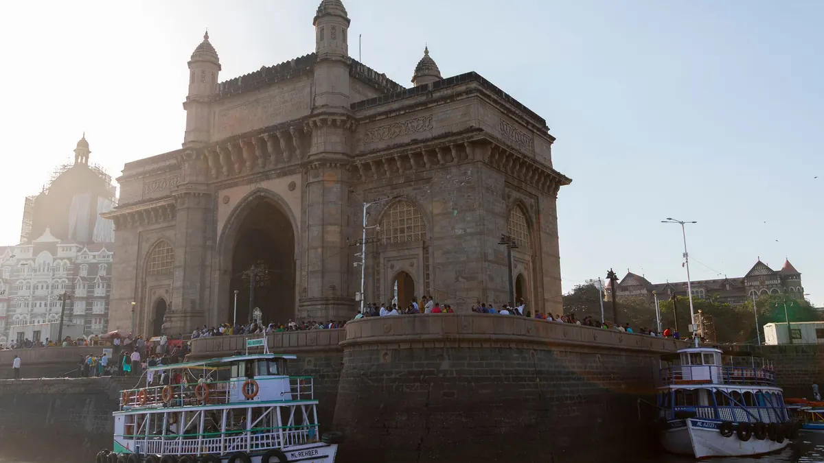 Stunning view of the iconic Gateway of India with boats and visitors at sunset in Mumbai.