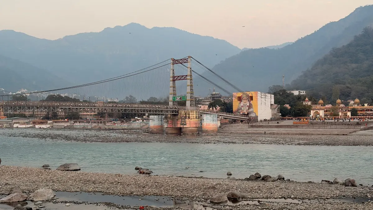 Laxman Jhula bridge spanning Ganges River in Rishikesh with mountainous backdrop.