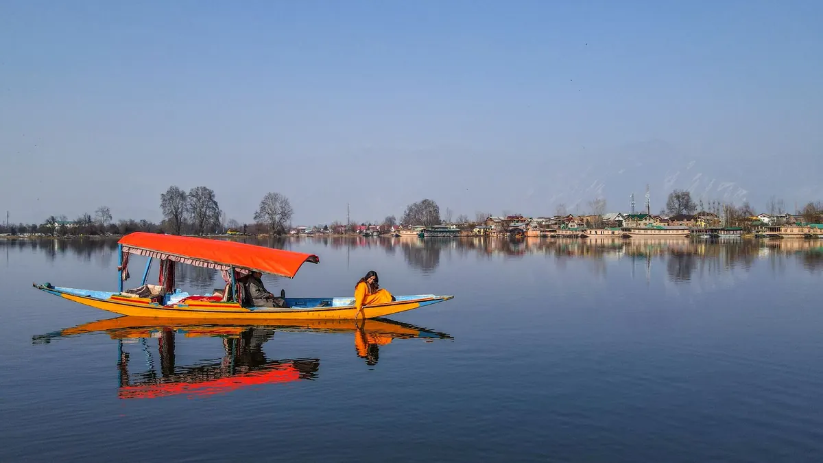 Colorful shikara boat with woman on Dal Lake, reflecting scenic beauty of Kashmir.
