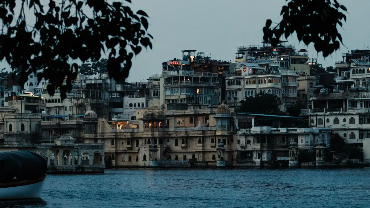 Scenic view of Udaipur's City Palace and surrounding architecture seen from Lake Pichola at dusk.