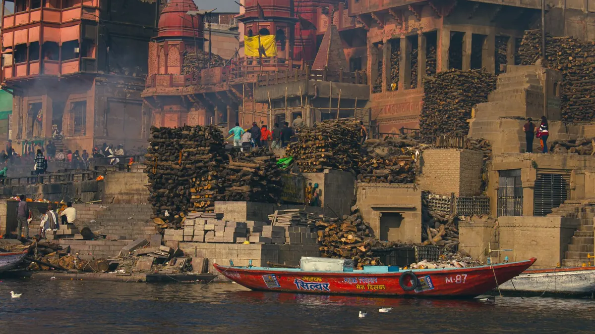 Colorful boats docked by ancient ghats with bustling urban scenery in the background.