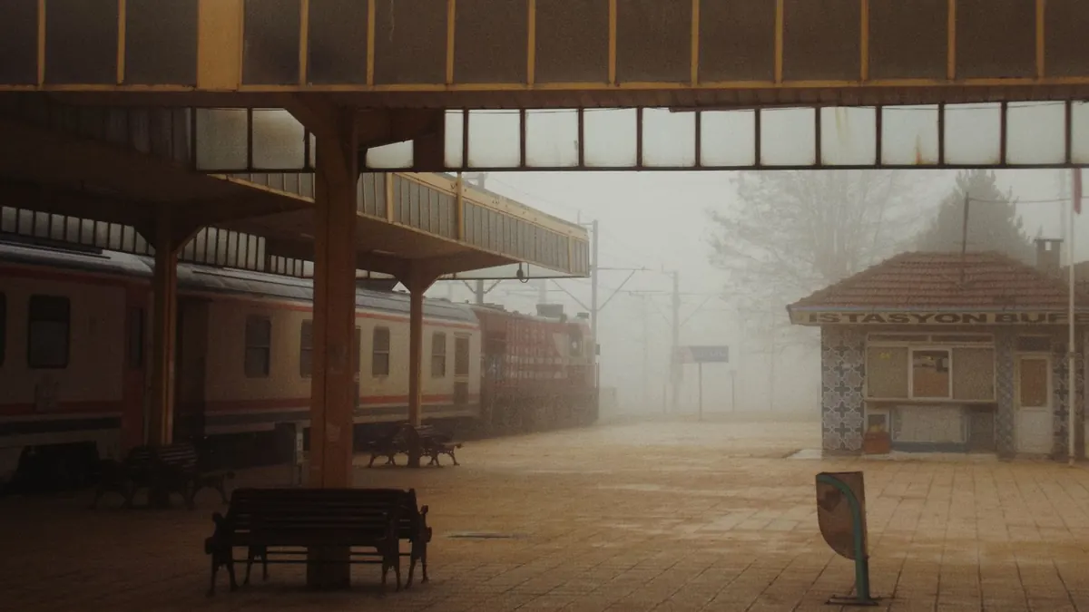 A foggy railway station featuring a train and empty benches on a misty day.