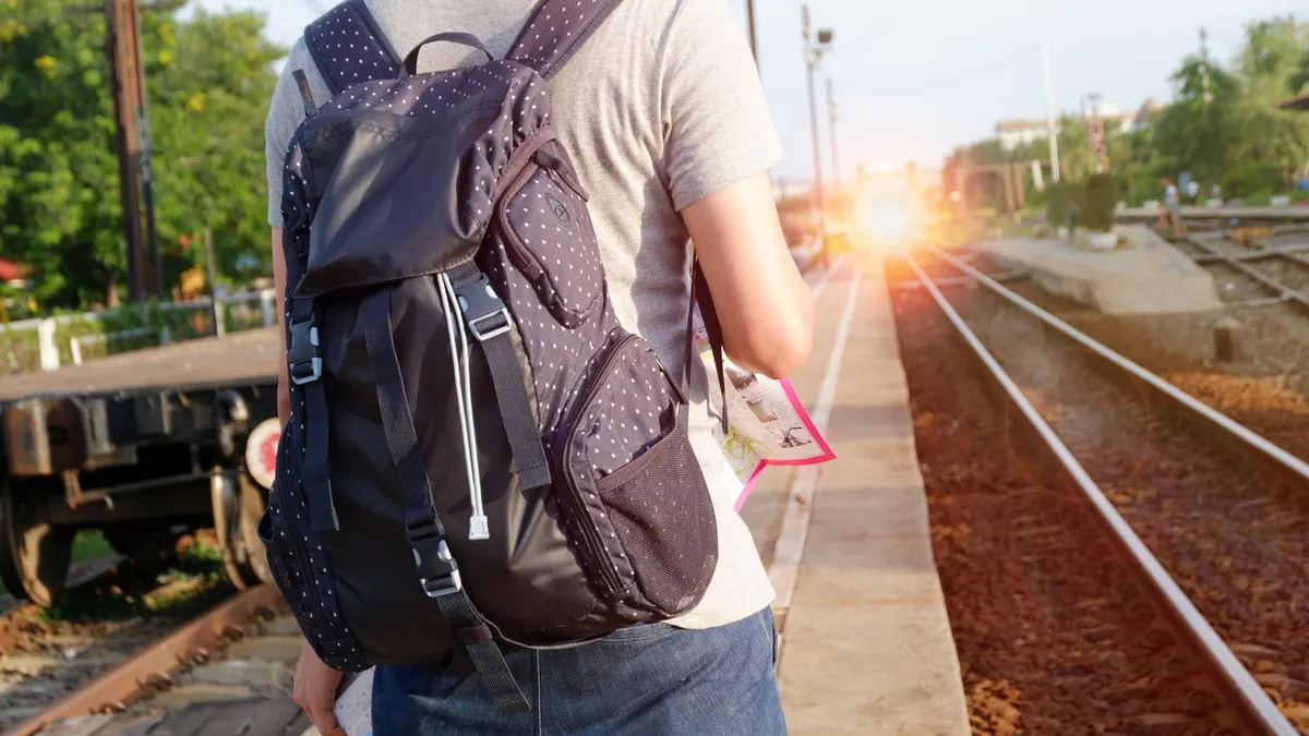 A person with a backpack waits at a railway station during daytime.
