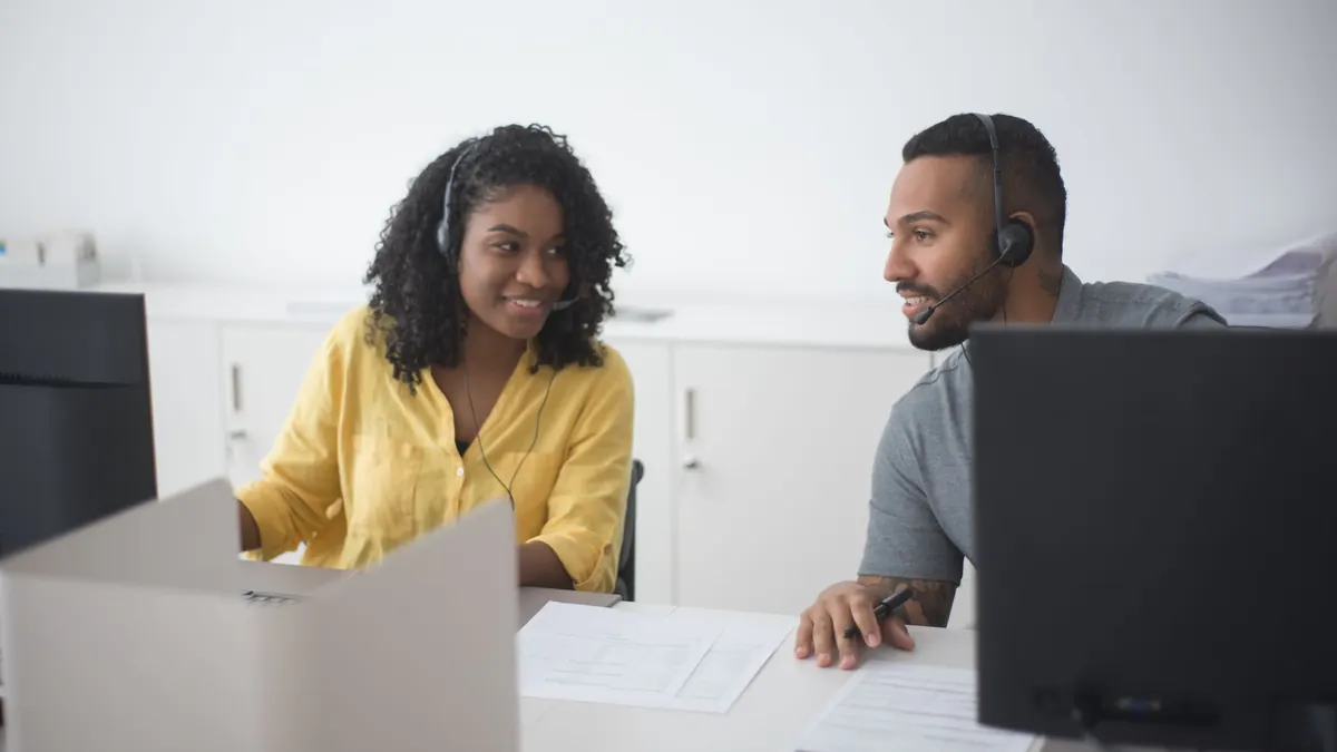 Two call center agents working together with headsets in a modern office environment.