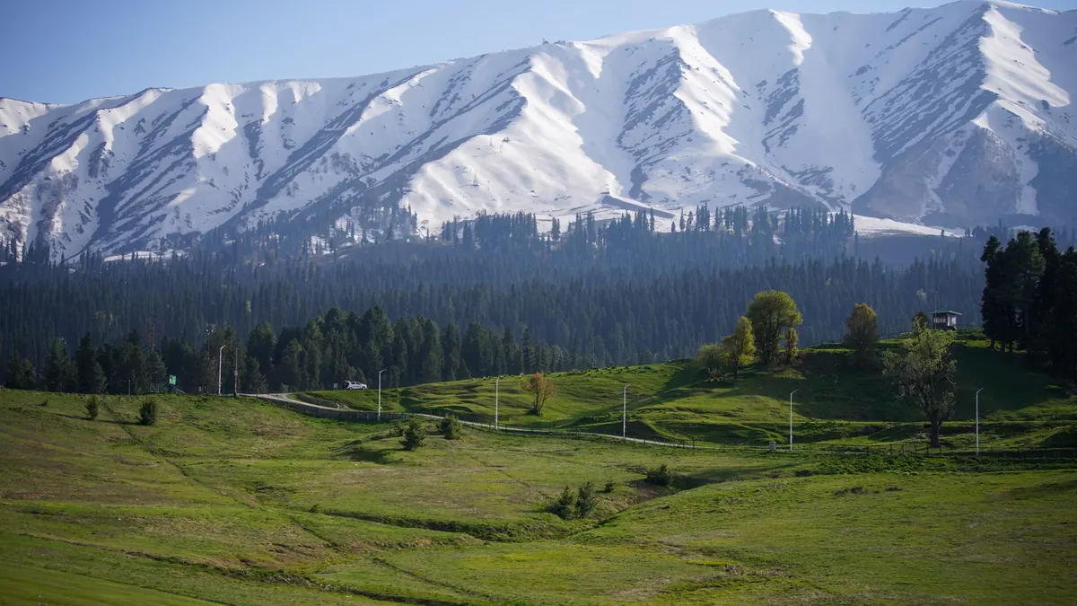 Gulmarg's verdant valley with majestic snowcapped mountains on a sunny day.