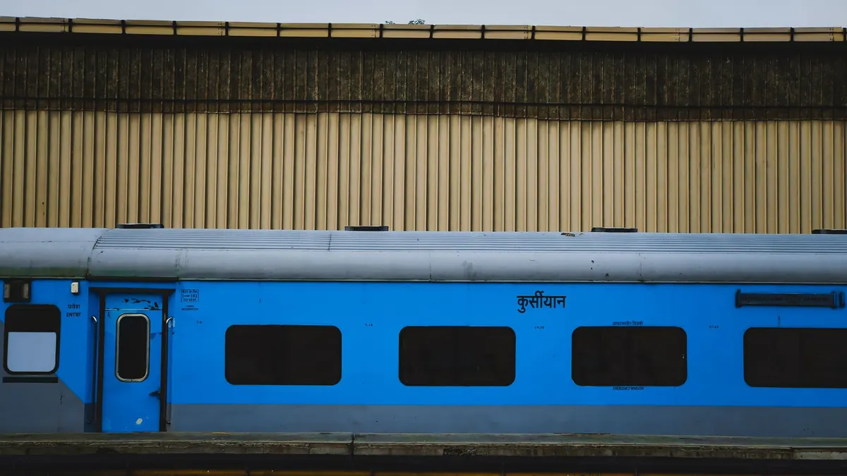 A blue passenger train waits quietly by an empty platform at a train station.