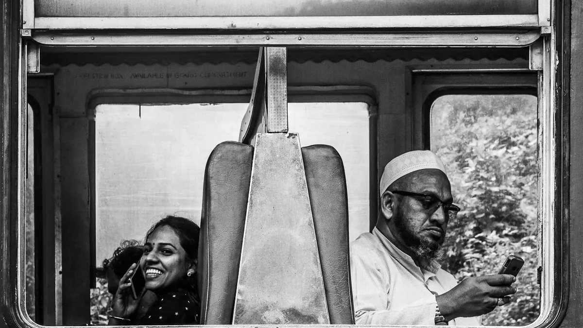 Black and white photo of two passengers in an Indian train, capturing a candid moment.